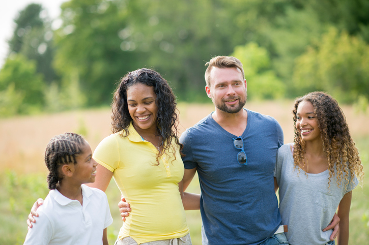 Una feliz familia de cuatro miembros se encuentra junta en un campo soleado, sonriendo y disfrutando de su tiempo al aire libre